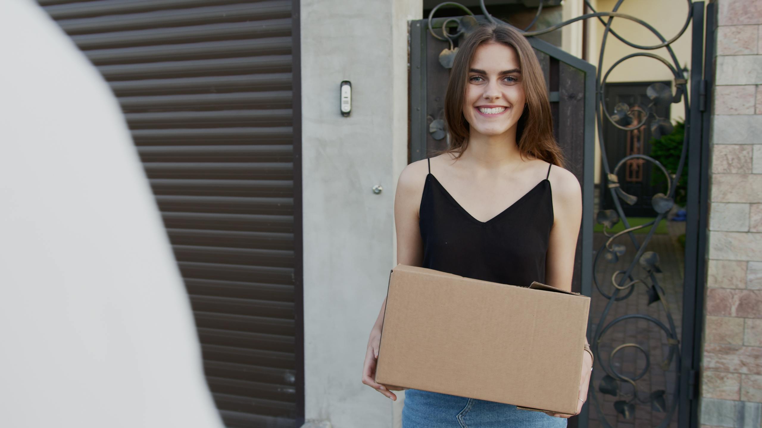 A cheerful woman holding a cardboard box, standing outside a building, showcasing a delivery service.